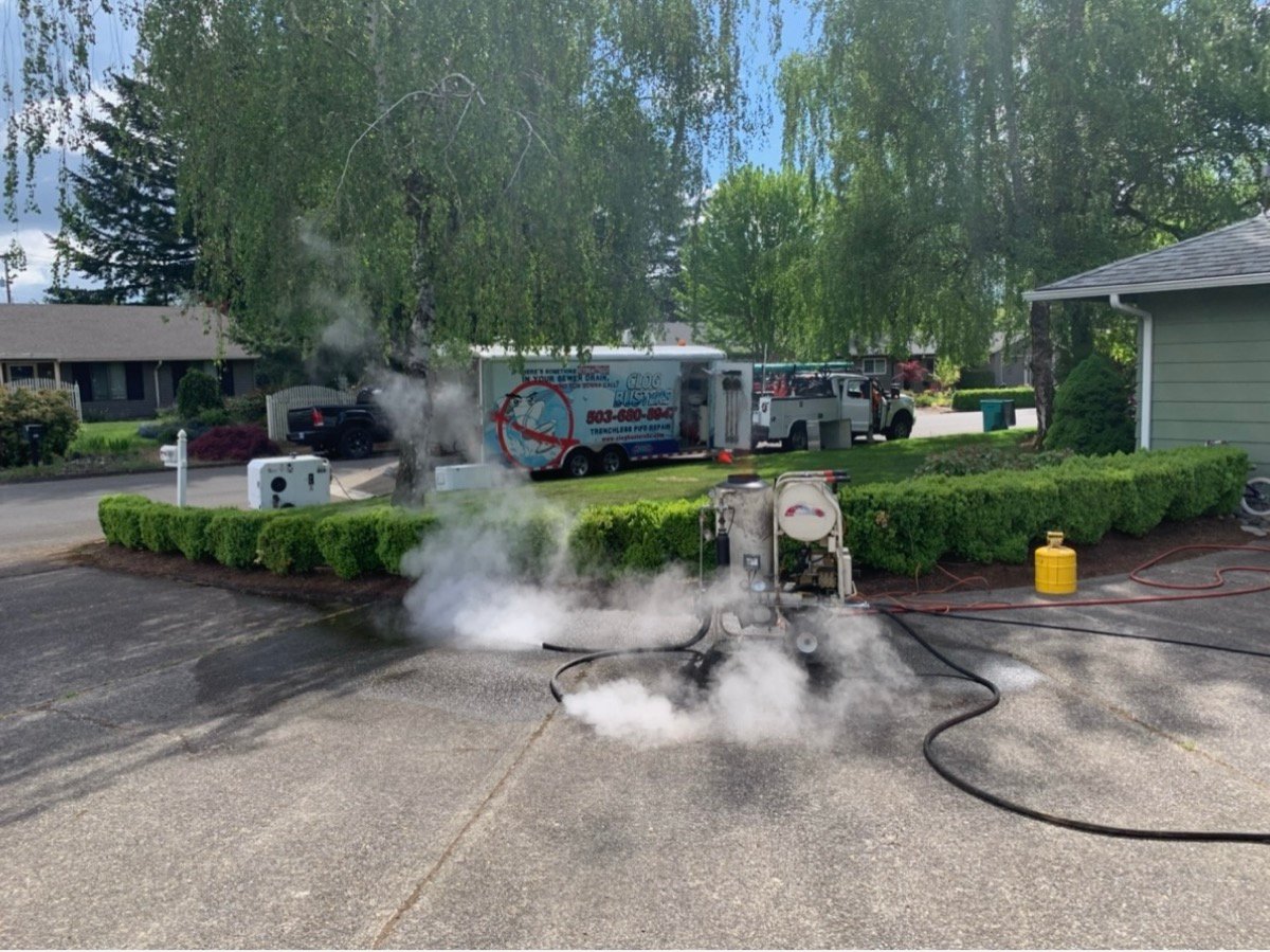 Steam rising during CIPP liner cure process at Cedar Hills Beaverton trenchless sewer repair with Clog Busters equipment trailer in background