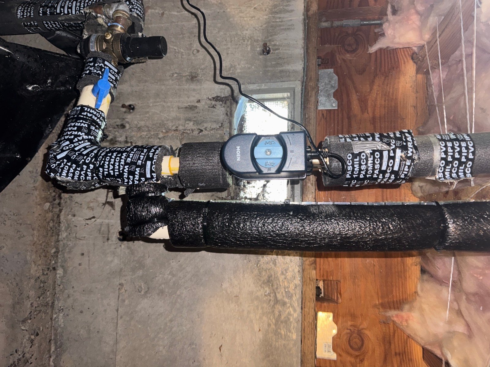 Moen Flo Smart Water Monitor and Shutoff installed on the main water line in a crawlspace, with pipe insulation reinstalled around it